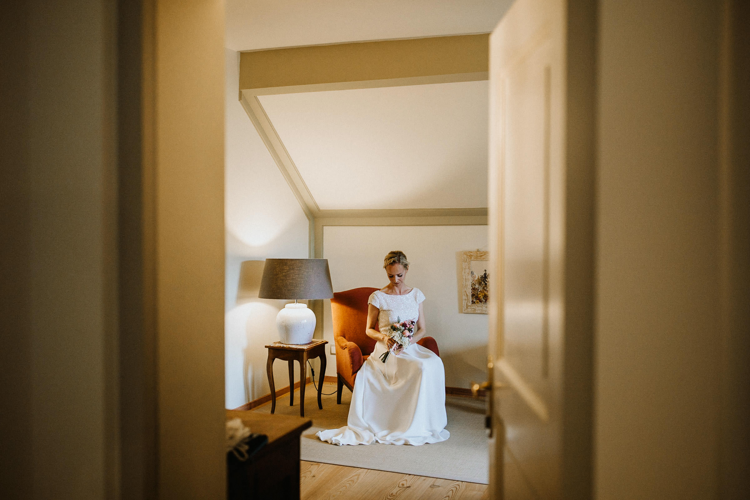 Schlosshochzeit: Blick durch eine halbgeöffnete Tür auf die Braut im Hotelzimmer im Sessel