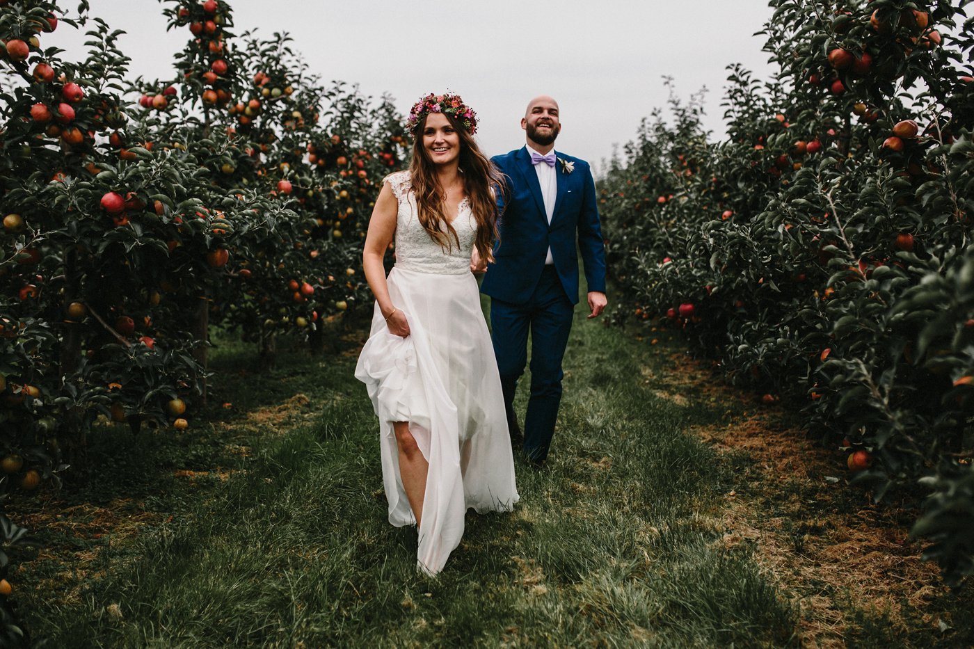 Urbane Hochzeit: Brautpaar läuft Hand in Hand durch Apfelbaum-Reihen